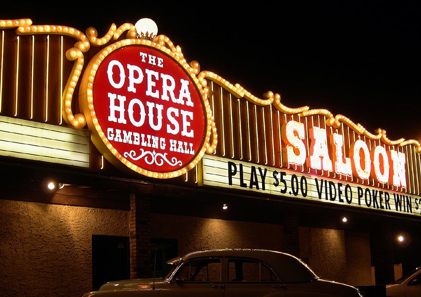 A neon sign on a building at night with a close-up of a parked car visible below it.