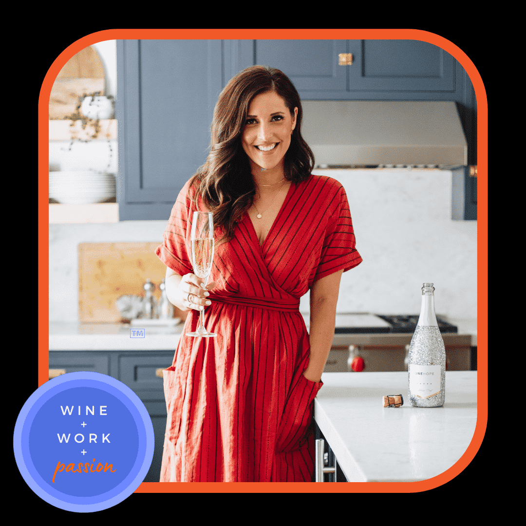 Napa Valley Wine Academy Wine Articles and Podcasts A woman in a red dress smiling and holding a glass of champagne indoors, with a bottle and cork visible in the background.