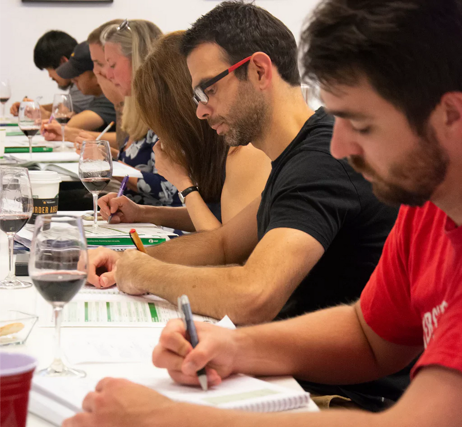 Students taking tasting notes at a bench of wine glasses during a WSET class at Napa Valley Wine Academy